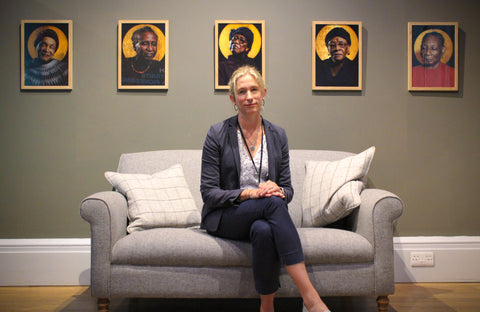 Ren Renwick sits on a grey sofa underneath a series of portraits of elderly Black women from the Evergreen Elders club in Bristol.
