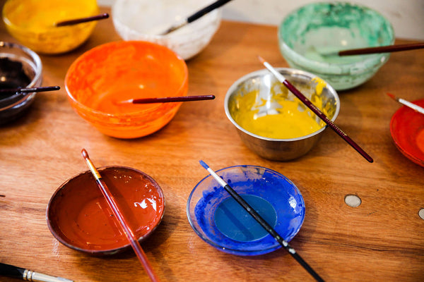 
      9 Small bowls of brightly coloured pigments made into paints with one thin brush resting across each bowl