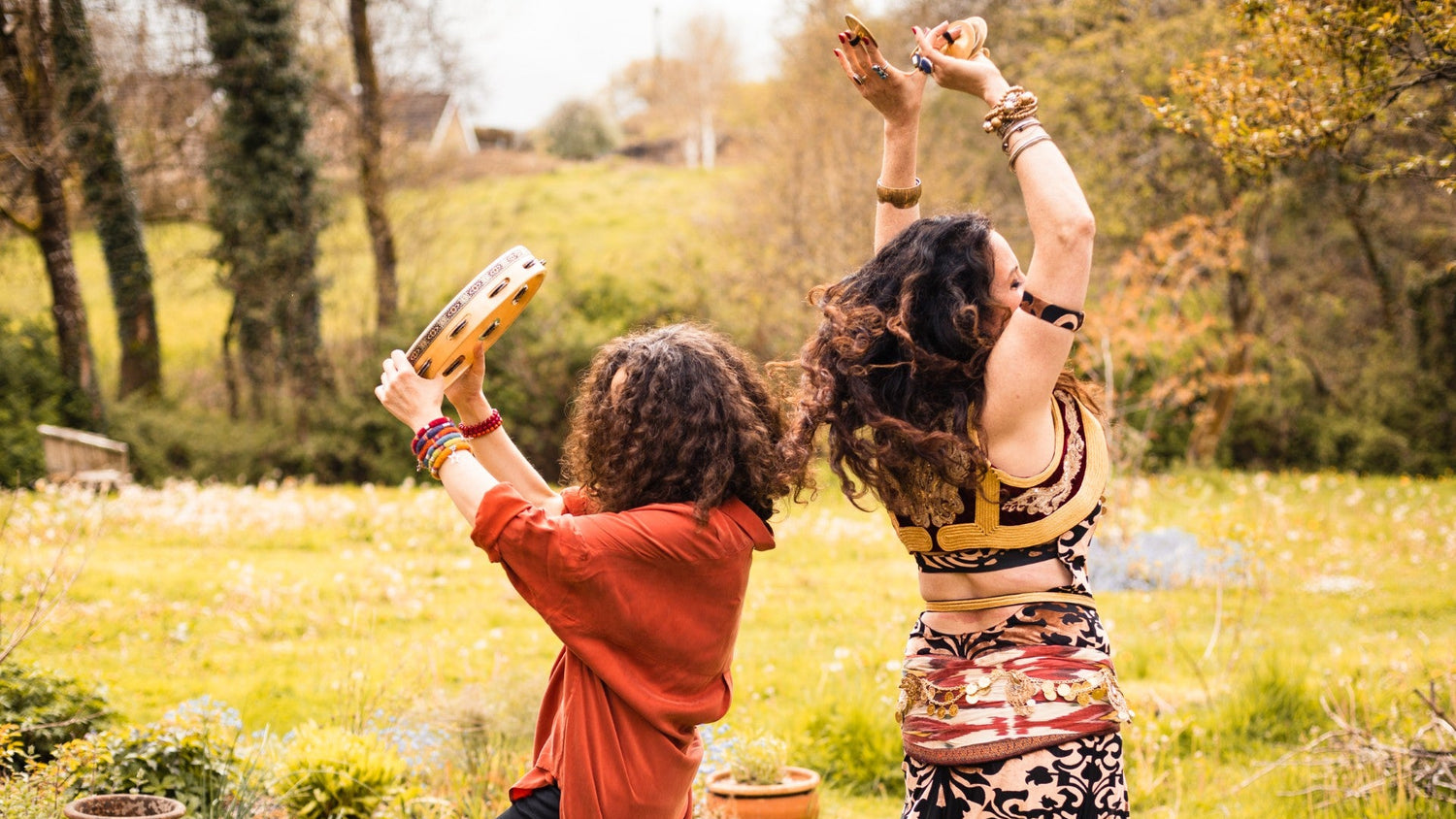 Two people dancing outdoors in a garden with trees and grass in the background.