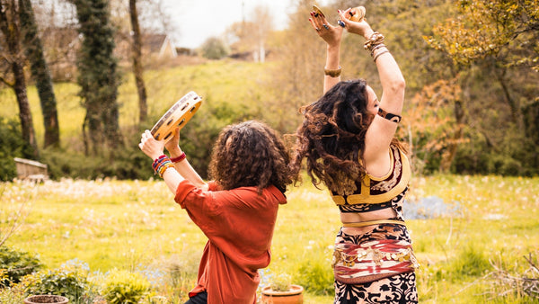 
      Two people dancing outdoors in a garden with trees and grass in the background.