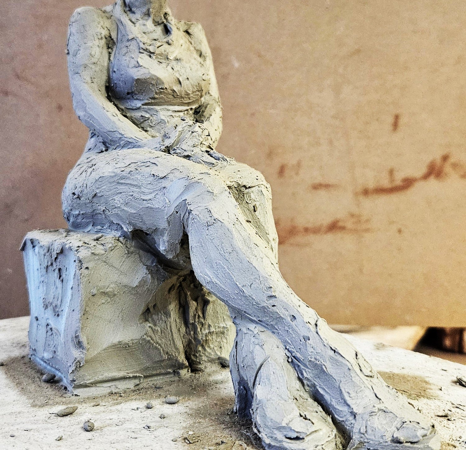 Clay sculpture of a seated figure on a wooden block with a plain background