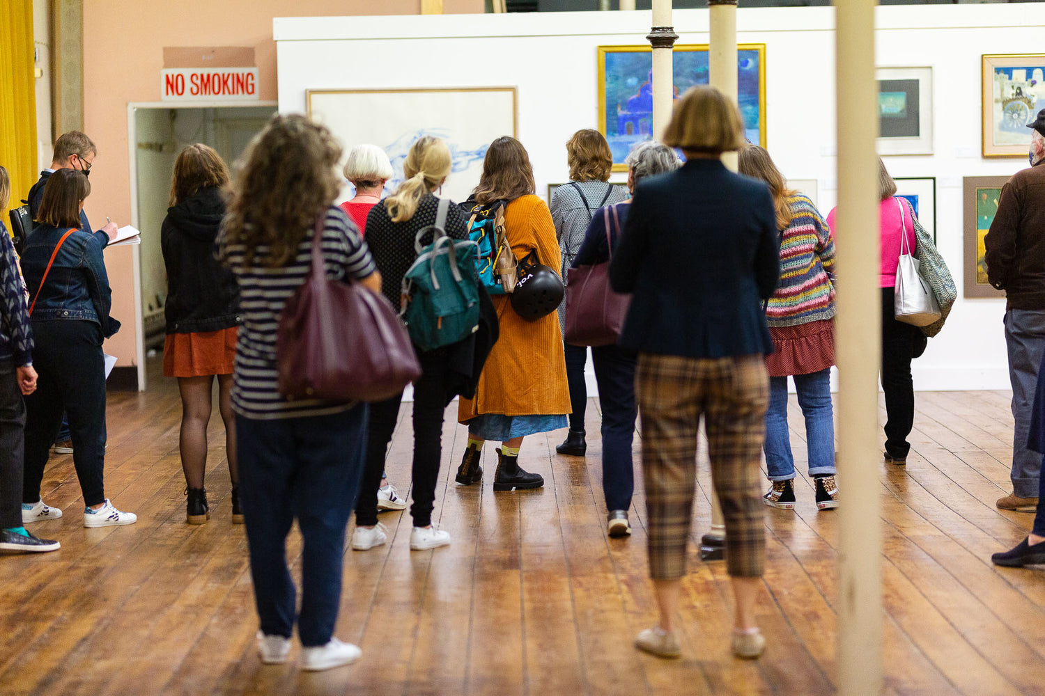 A group of people stand facing forward in a gallery space viewing artworks 