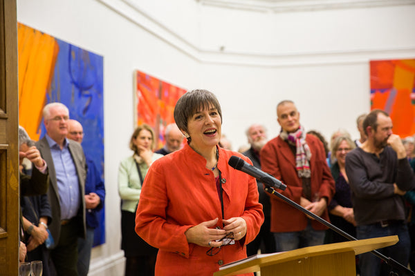 RWA Albert Irvin exhibition preview, 2018. RWA Director speaking to a microphone with people in the background of a busy gallery space  